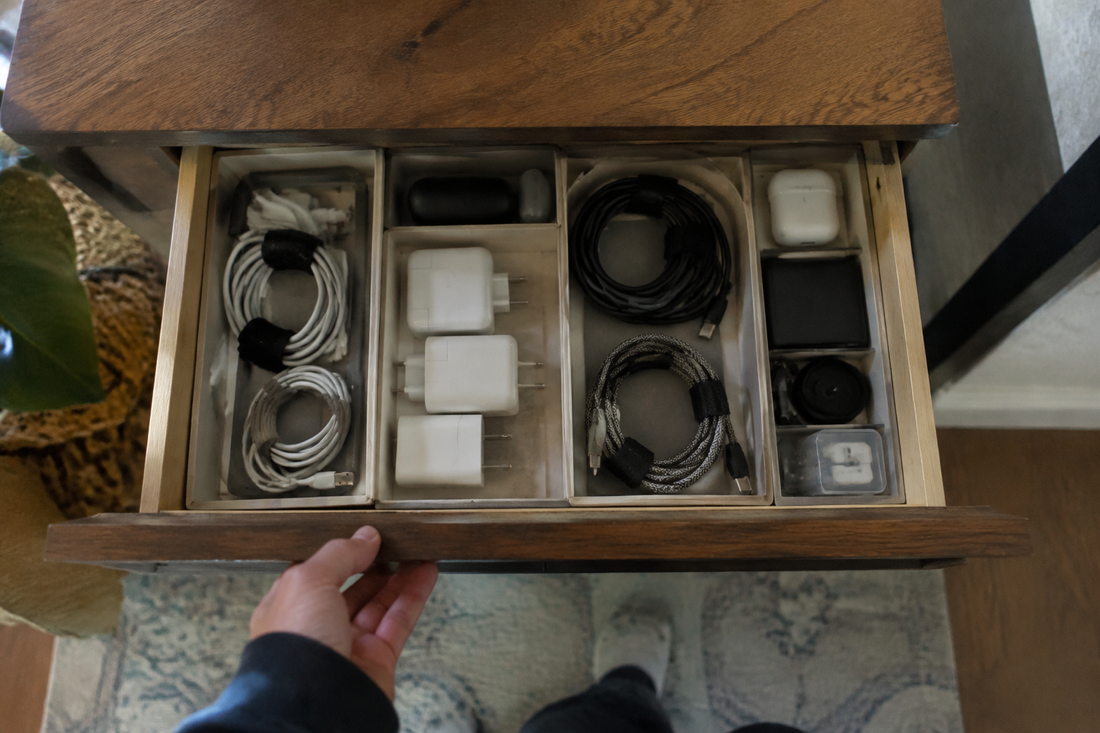 A hand opens a wooden tech drawer with cables and adapters arranged in separate compartments