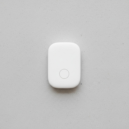 White Bluetooth item finder tracker tag on light grey concrete surface, compact 27x44mm rounded rectangular form, single button face, studio lighting
