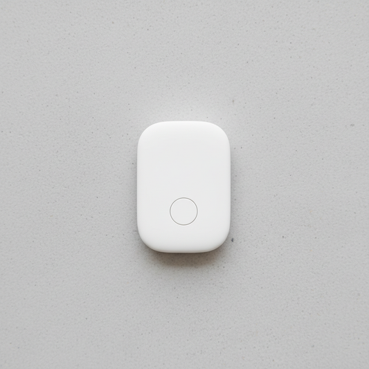 White Bluetooth item finder tracker tag on light grey concrete surface, compact 27x44mm rounded rectangular form, single button face, studio lighting