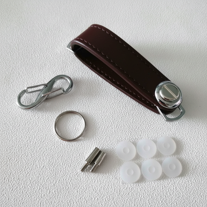 Red leather key organizer keychain with chrome carabiner clip, screw posts, key ring, and silicone pads on grey concrete surface