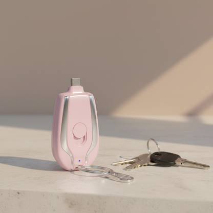 Mini keychain power bank in pink with built-in USB-C connector and carabiner clip, resting on pale stone surface with natural lighting